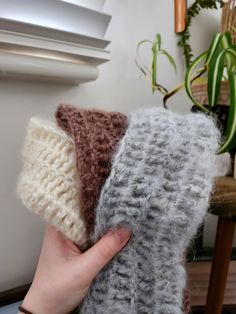 a person holding three different colored knitted items in their hands, one is white and the other is brown