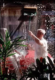 a woman standing in front of a window with rain coming down on her and plants