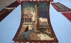 a person holding up a rug on top of a blue tablecloth covered in pictures