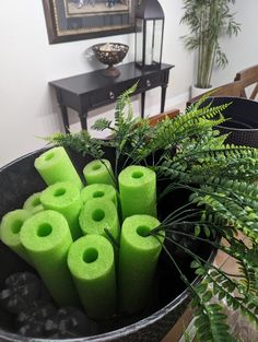 green candles are in a black bowl on a table next to plants and a mirror