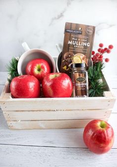 a wooden crate filled with apples and spices next to an apple cider on a table