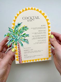 two hands holding up a cocktail bar menu with a palm tree on the front and bottom