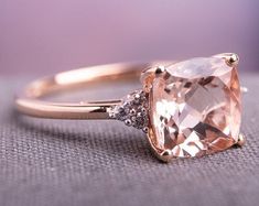 an engagement ring with a pink diamond and two diamonds on the side, sitting on top of a gray cloth