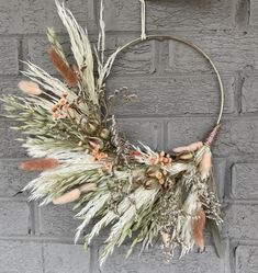 a wreath hanging on the wall with dried flowers and leaves in front of a brick wall