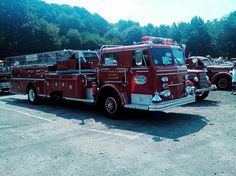 an old red fire truck parked in a parking lot next to other cars and trees