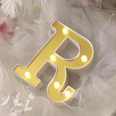 the light up letter p is sitting on top of white tulle with flowers around it