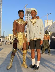 two men standing next to each other wearing gold costumes and headgear, one with his arm around the other's neck