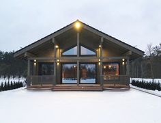 a small wooden cabin with lights on the front porch and windows in the snow covered yard