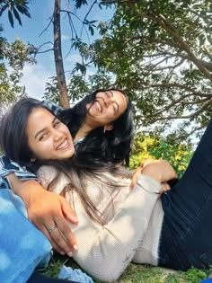 two women are laying on the grass and one is holding her arm around the other