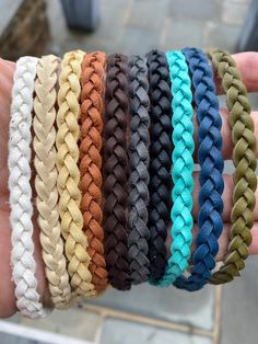 a hand holding five different colored braided bracelets