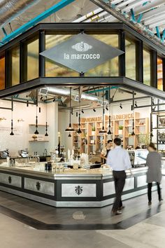 two people walking in front of a store called la marzocco with lots of windows