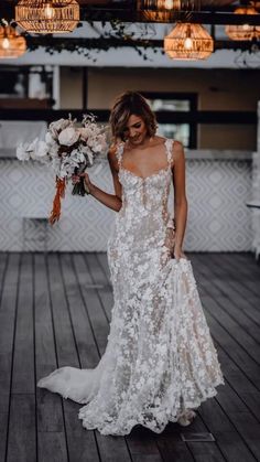 a woman in a white wedding dress holding flowers and looking down at the floor with lights above her