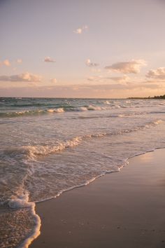 the ocean waves are rolling in and out onto the beach at sunset with clouds overhead