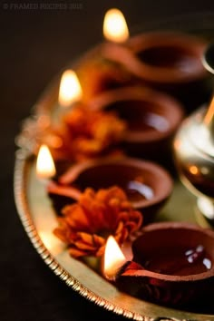 candles are lined up on a plate with flowers in the middle and one candle is lit