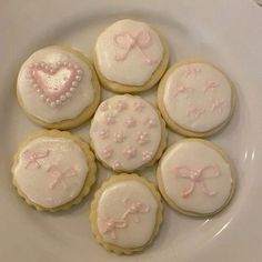 six decorated cookies on a white plate with pink bows and hearts in the shape of heart