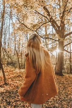 a woman standing in the woods with her back to the camera and looking at trees