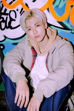 a young man sitting in front of a graffiti covered wall