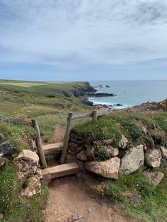 a wooden bench sitting on top of a lush green hillside next to the ocean with rocks and grass