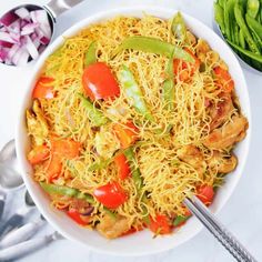 a bowl filled with noodles and vegetables next to some spoons on a white table