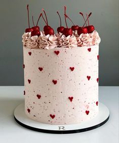 a white cake with pink frosting and red hearts on the top is topped with cherries