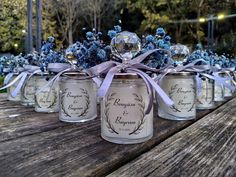 several jars with blue flowers are sitting on a wooden table and tied in purple ribbon