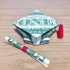 a money origami graduation cap and two red tassels on a wooden table