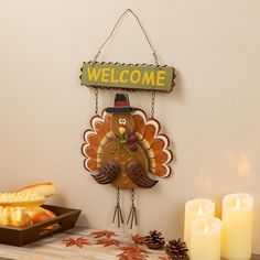 a wooden sign that says welcome with a turkey hanging from it's side next to bread and candles