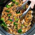 a person is stirring broccoli and chicken in the crock pot with tongs