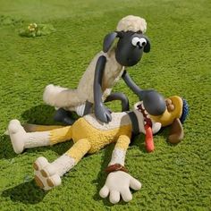 a sheep laying on the ground next to a toy man with a carrot in his mouth