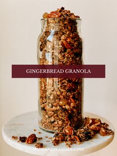 a glass jar filled with granola sitting on top of a white table next to a pile of nuts