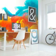 a room with a desk, chair and bike in front of a colorful wall mural