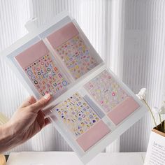 a person holding up some stickers on top of a table next to a book