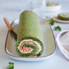 there is a roll with meat and spinach in it on a plate next to a knife