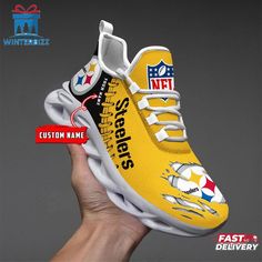 a hand holding up a yellow and white shoe with pittsburgh football on the soles