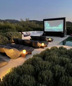 an outdoor movie is set up in the middle of a garden with lounge chairs around it