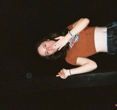 a woman in brown shirt and black shorts standing on skateboard with her hand up