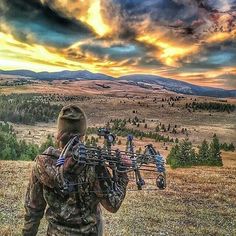 a man with a bow is standing in the grass and looking out at the mountains