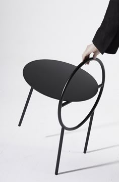 a person standing next to a black table on top of a white floor with their hand on the edge