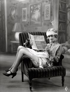 an old photo of a woman sitting in a chair reading a newspaper with her legs crossed