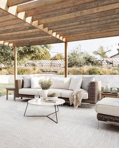 an outdoor living room with white furniture and wood pergolated roof over the patio