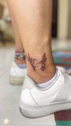 a small tattoo on the ankle of a woman's foot, with two birds flying above