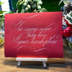 a red card with white writing on it sitting on a table next to some flowers