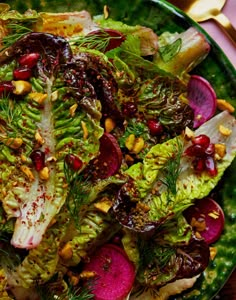 a green plate topped with lettuce, radishes and pine nuts on top of a wooden table