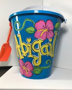 a blue bucket with flowers painted on it and a red spatula in the background