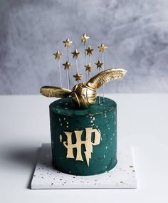 a green cake with gold stars on top and a bird decoration in the shape of an h