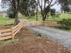 a wooden fence on the side of a dirt road next to a field and trees