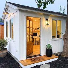 a small white house sitting next to a tree in front of a wooden door and window