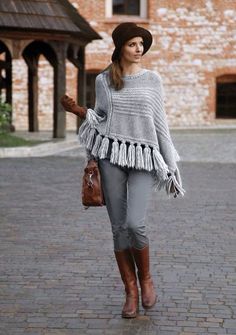 a woman walking down a brick road wearing a hat and sweater with tassels