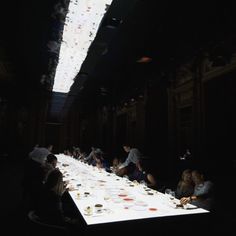 people are sitting at a long table with plates and cups on it in the dark