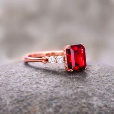 an engagement ring with a large red stone surrounded by small white diamonds on top of a rock